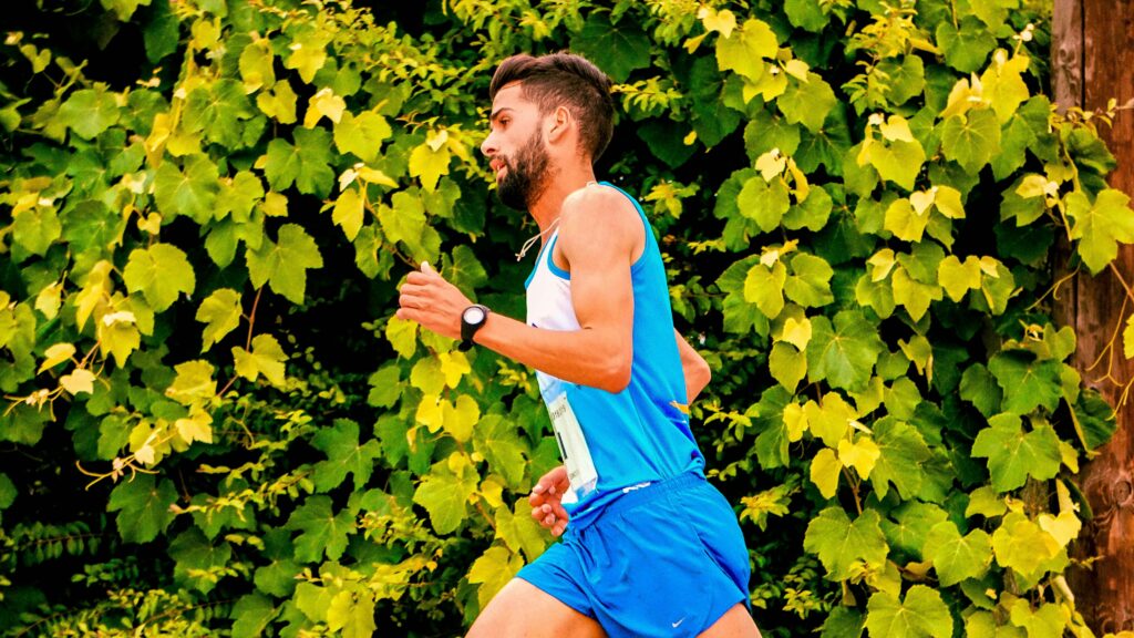 A man jogging outdoors beside vibrant green leaves, embodying fitness and energy.